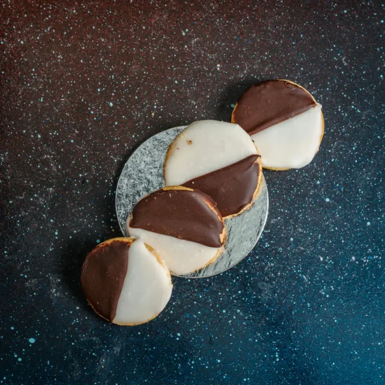 Four black and white cookies with half vanilla and half chocolate glaze, diagonally frosted and stacked in a line on a silver plate.