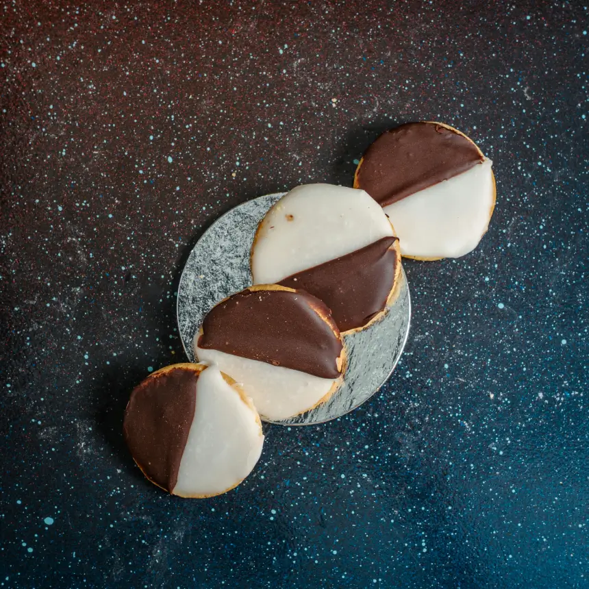 Four black and white cookies with half vanilla and half chocolate glaze, diagonally frosted and stacked in a line on a silver plate.