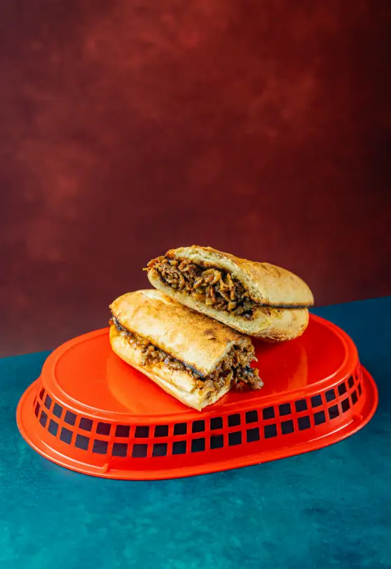Philly cheesesteak-style sandwich with shaved beef and sautéed onions inside a toasted hoagie roll, served on a flipped red basket