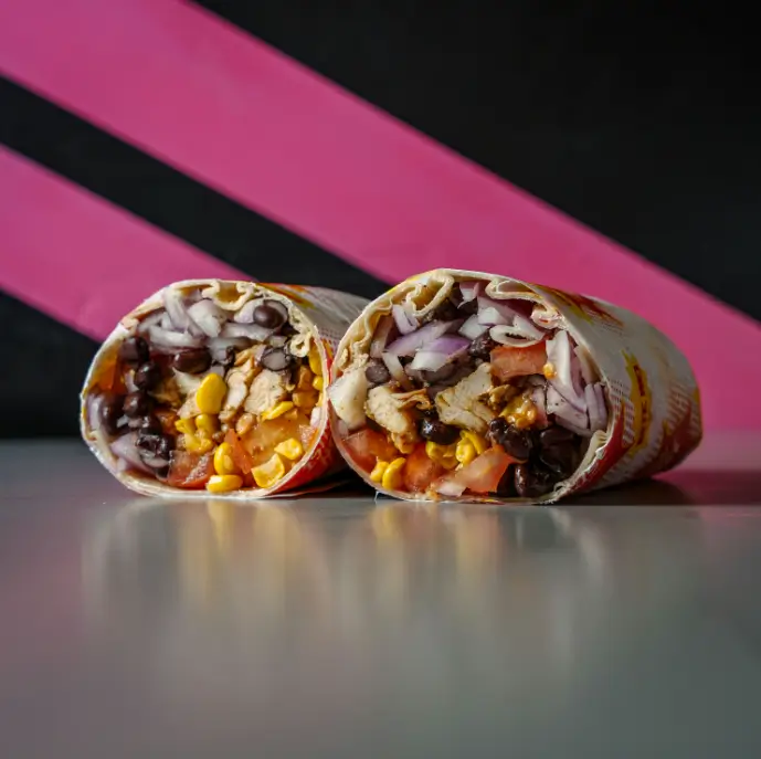 Southwestern-style wrap cut in half, filled with grilled chicken, corn, black beans, diced tomato, and chopped red onion, wrapped in branded Smash House paper