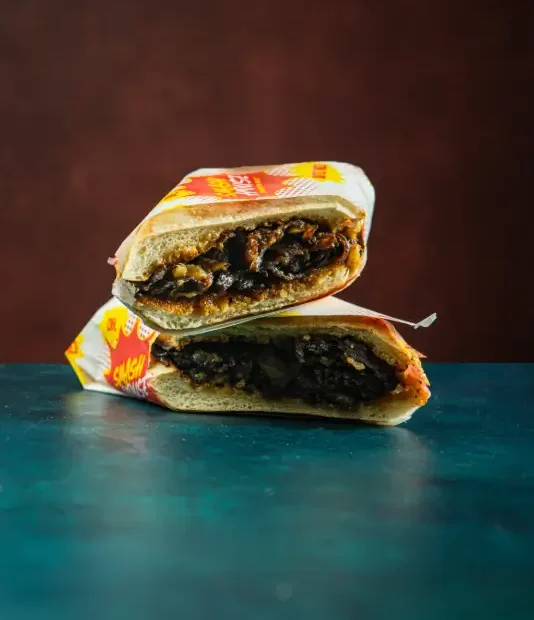 Mushroom melt sandwich split in half, loaded with grilled mushrooms and onions inside a soft roll, wrapped in bold Smash House comic-style paper