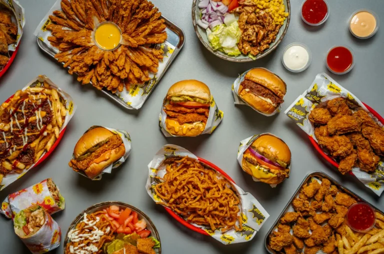 Overhead flat lay of Smash House feast featuring burgers, chicken wings, blooming onion with dip, seasoned fries, chicken wraps, crispy tenders, salads, and dipping sauces