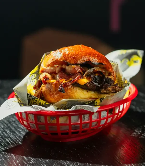Smash burger with beef bacon, grilled onions, and vegan cheese in a glossy toasted bun, served in a red basket with Smash House branded wrap
