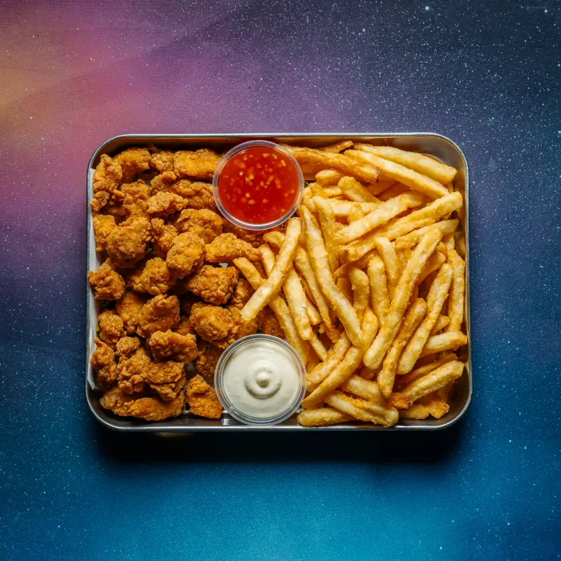 Tray of crispy fried chicken bites and golden French fries with two dipping sauces, set against a vibrant galaxy-themed background